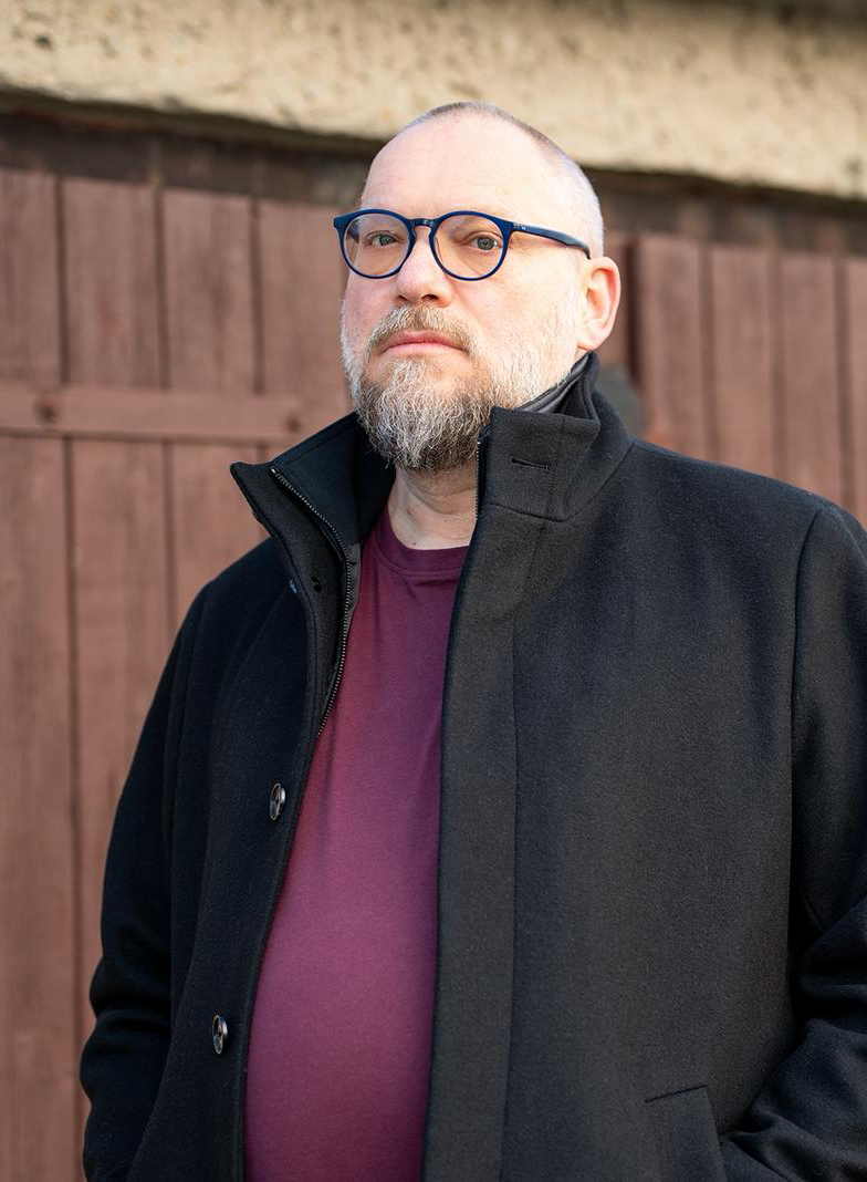 Ein Mann im schwarzen Mantel vor einer Garage